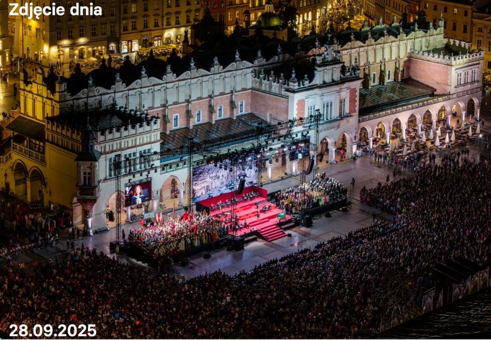 Duży tłum gromadzi się nocą na Rynku Głównym w Krakowie na plenerowym wydarzeniu Teatru KTO w pobliżu oświetlonych Sukiennic, ze sceną wyłożoną czerwonym dywanem i wieloma widzami. Tekst w języku polskim wskazuje datę: 28.09.2025.