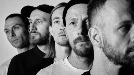 Pięciu mężczyzn stoi w jednej linii, zwróceni w tym samym kierunku z poważnymi wyrazami twarzy. Czarno-białe zdjęcie podkreśla ich cechy i kontrasty, nadając dramatyczny, artystyczny charakter przypominający surowe emocje występujące na pustyni. Pięciu mężczyzn stoi w jednej linii, zwróceni w tym samym kierunku z poważnymi wyrazami twarzy. Czarno-białe zdjęcie podkreśla ich cechy i kontrasty, nadając dramatyczny, artystyczny charakter przypominający surowe emocje występujące na pustyni.